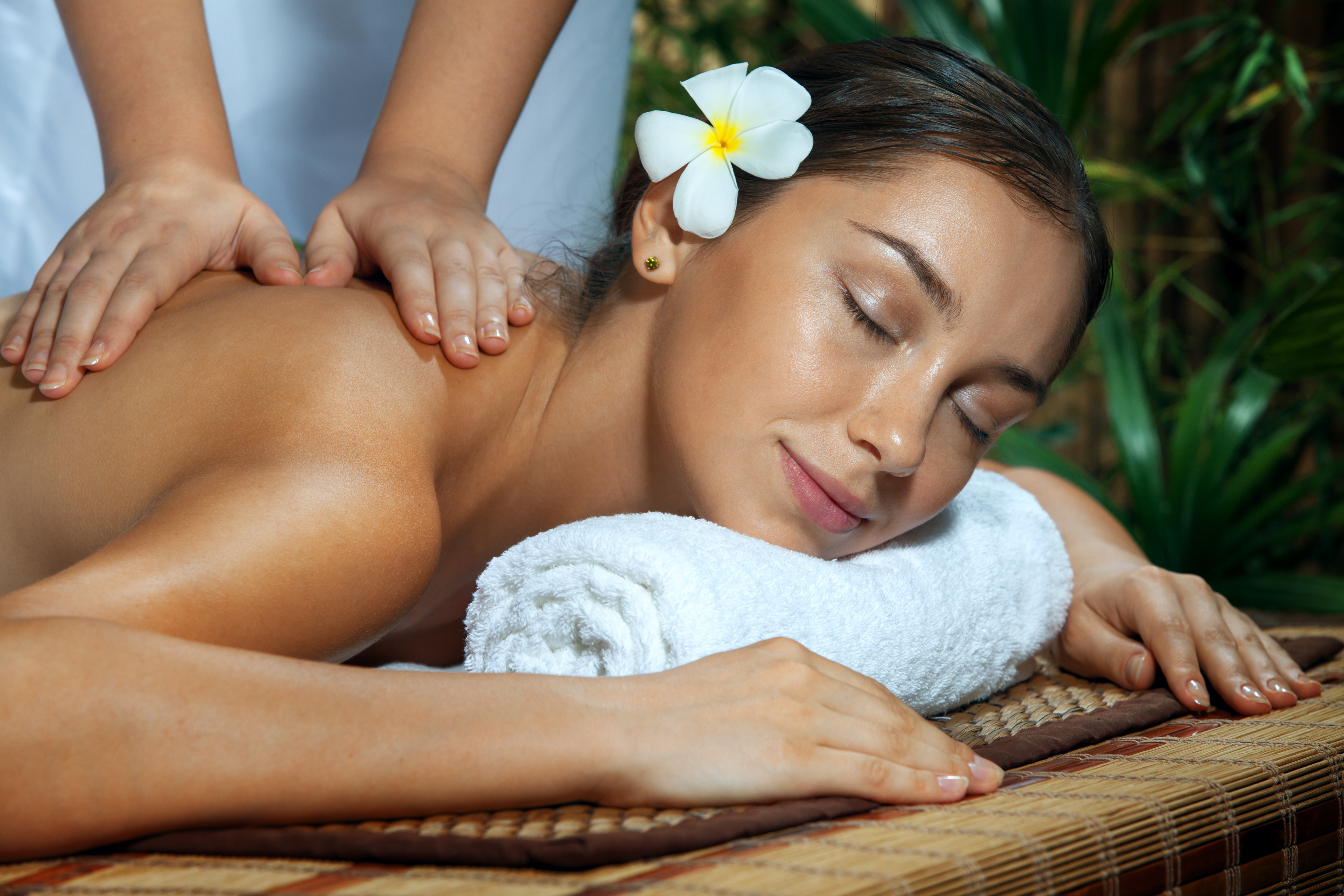 A woman with a flower behind her ear receving a massage.