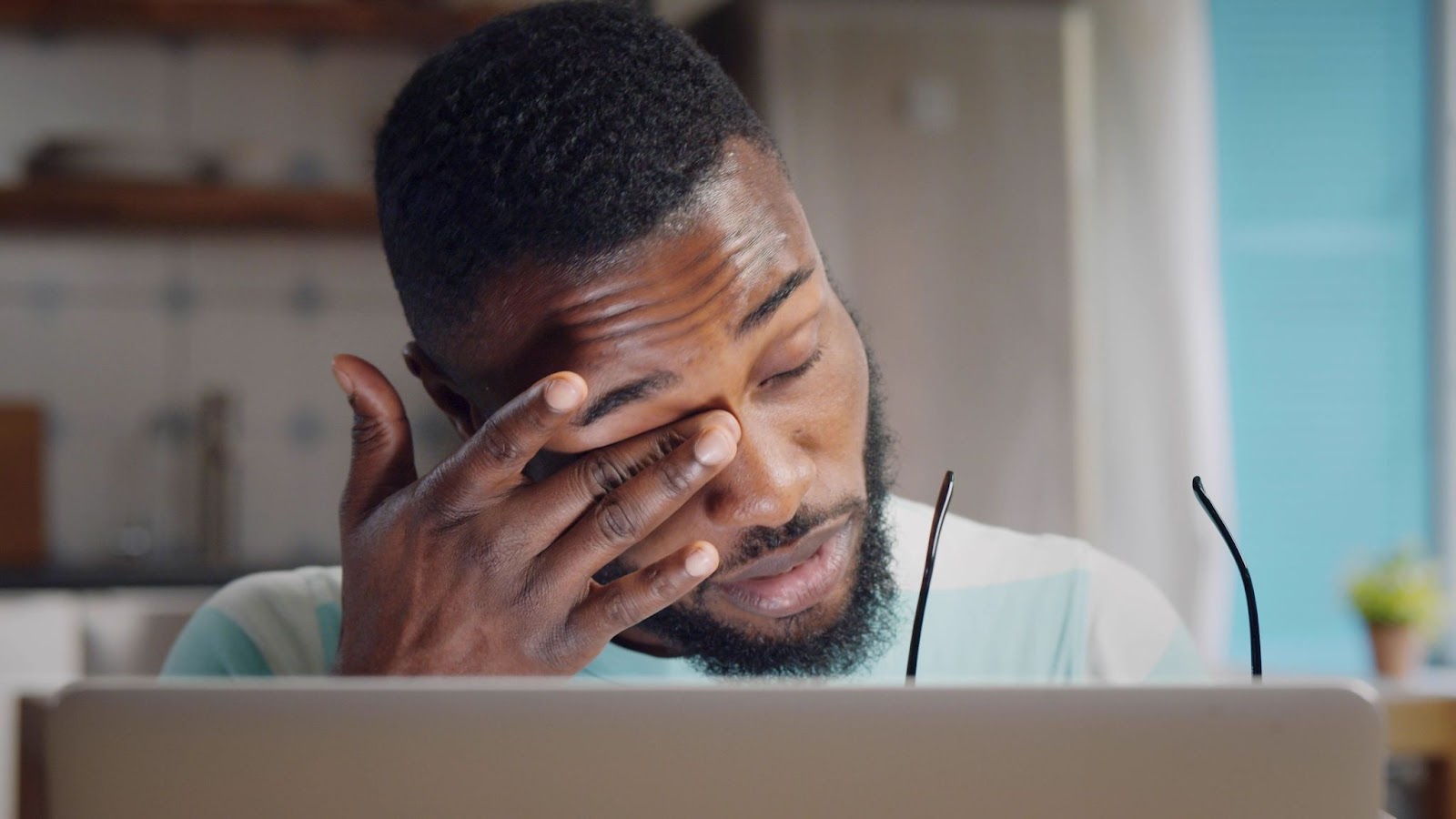man working at his computer and rubbing his eyes because he's tired and stressed